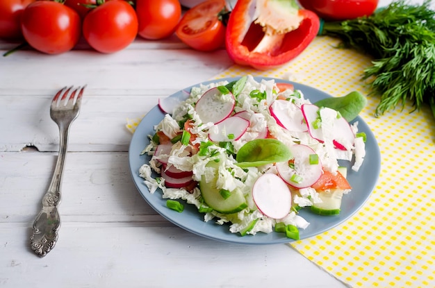 Spring tasty fresh salad with tomatoes, cucumbers, radishes, onions, herbs seasoned with vegetable oil in plate on old darkwhite wooden  background with natural light. copy space