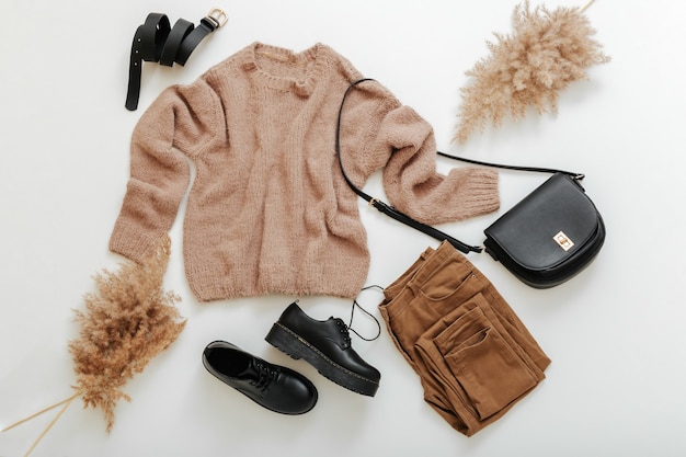 Spring winter autumn woman outfit. fashion basic female clothes set in beige brown colour. Cloth and shoes casual style with knitted sweater and reed Pampas branches. Flat lay clothes on white.