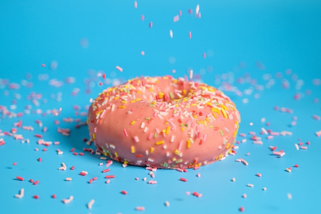 Sprinkles falling from top on Tasty pink strawberry donut. Delicious dessert on blue background.