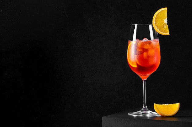 Spritz Cocktail in wine glass with ice and orange slice on dark background