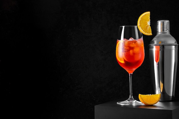 Spritz Cocktail in wine glass with shaker and orange slice on dark background