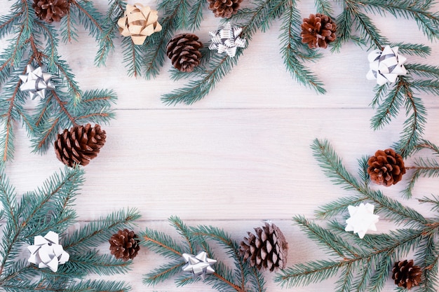 Spruce branches decorated with gold and silver bows and cones are arranged in a circle on a light wooden background.