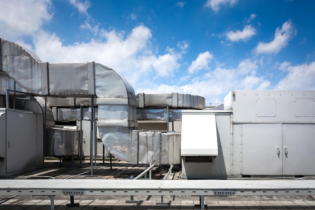 Square airconditioning unit on the roof with a round fan In the background gradually receding other units that are out of focus On the right side light blue sky and commercial space