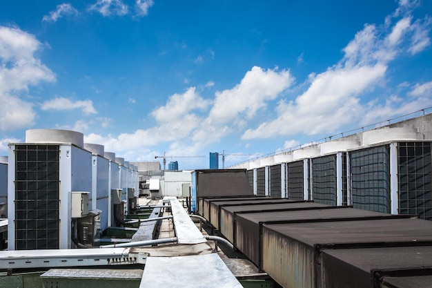 Square airconditioning unit on the roof with a round fan In the background gradually receding other units that are out of focus On the right side light blue sky and commercial space