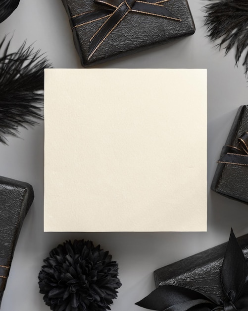 Square blank card between Wrapped Gift Boxes black paper flowers and feathers mockup