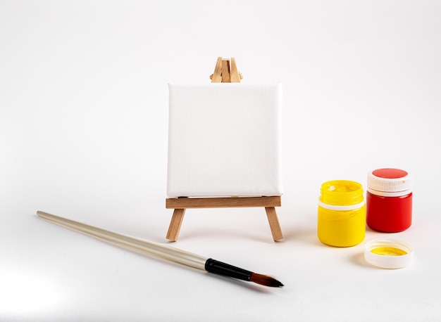 Square canvas blank paper on wood tripod easel painbrush and gouache paints in jars