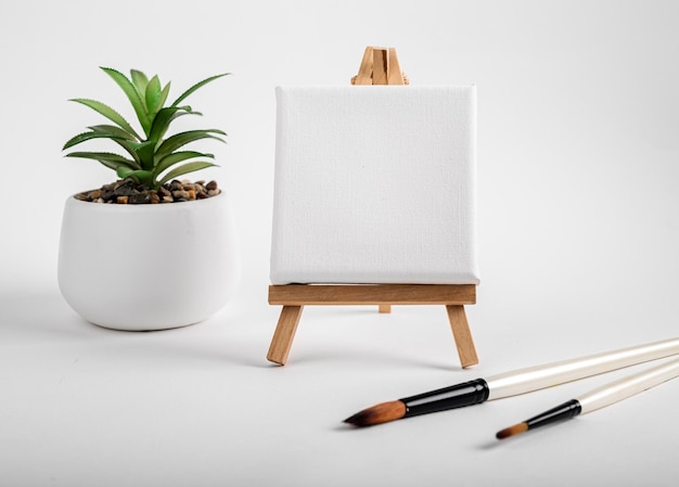 Photo square canvas on wood mini easel blank mock up on wood tripod paintbrushes and potted plant composition