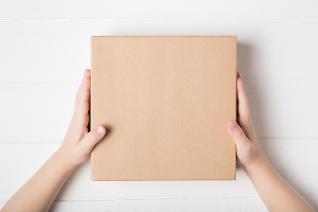 Square cardboard box in children hands. Top view, white background