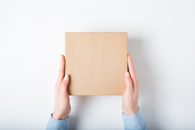 Square cardboard box in female hands, Top view, 