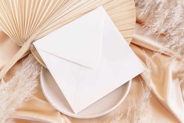 Square envelope on plate on dried palm leaf and beige silky fabric close up mockup