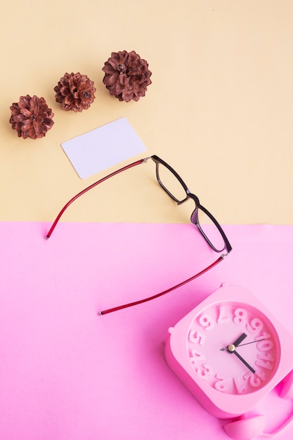 Square glasses, alarm clock, pine tree flowers on a pastel pink and pastel yellow background. Summer Concept, Minimal Concept