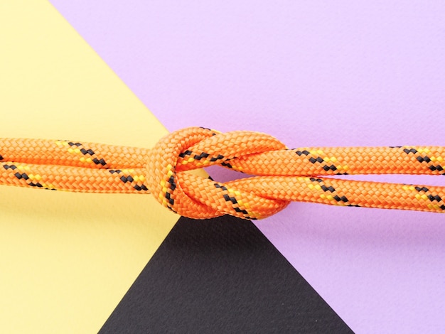 Photo a square knot made of nylon orange rope on a pastel purple background.