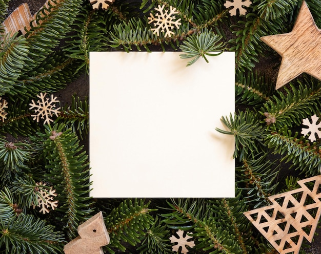 Square paper card between rustic wooden Christmas decorations and green fir branches