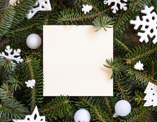 Square paper card between white Christmas decorations and green fir branches