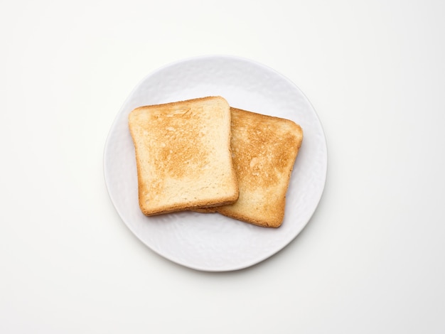 Square pieces of toasted bread made from white wheat flour on a round plate. White table background