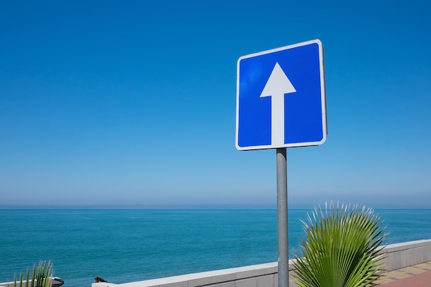 Square road sign with white arrow on blue sky background