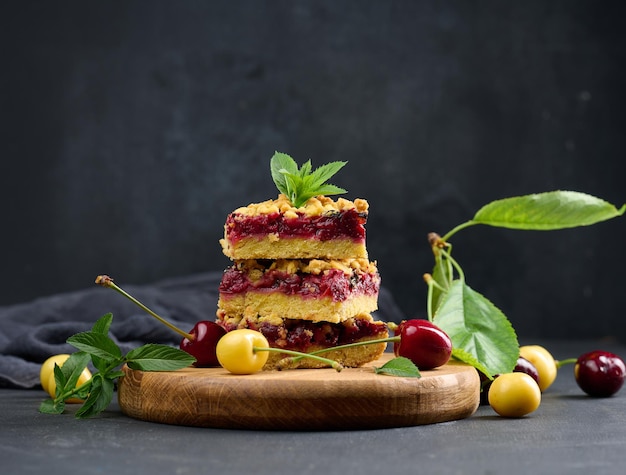 Square slices of cherry crumble lie in a stack on a black board