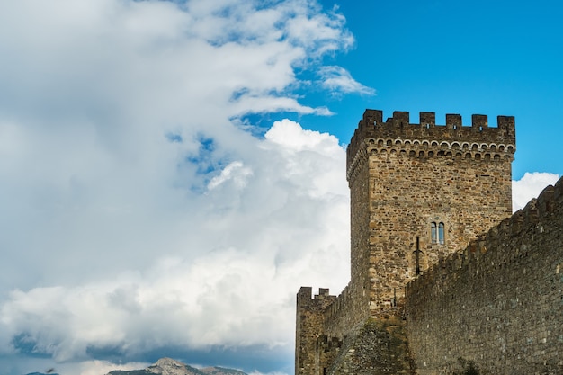 square tower of an ancient fortress with blue sky and clouds.