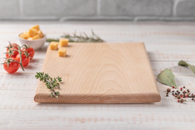 Square wooden cutting board with cherry tomatoes cheese and spices on a white background mockup with copy space for text side view