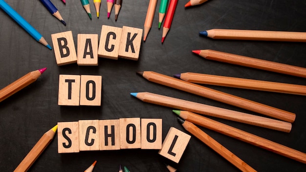 Square wooden letters with the phrase quotBack To Schoolquot written in English on a black chalkboard background and next to colored pencils