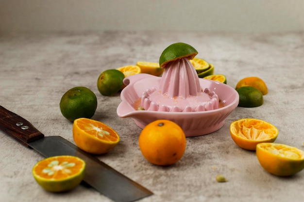 Squeezing Juice from Orange on a Manual Ceramic Squeezer. Set on a Rustic Table with a group of Small Oranges.