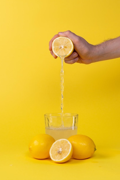 Squeezing lemon juice into glass on yellow background