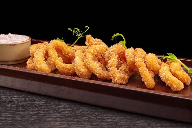 Squid rings in batter with sauce on a wooden board