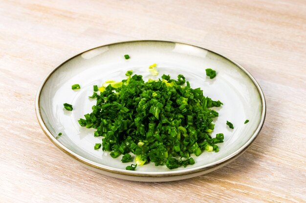 Squid salad with egg, green onion Step-by-step recipe step 4 cutting ingredient on grey blue plate on white wooden table. Close up. Selective focus. Copy space