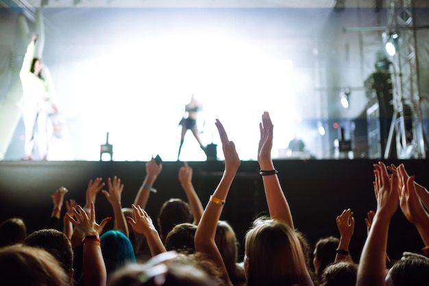 Srowd with raised hands at music festival Fans enjoying rock concert with light show clapping hands