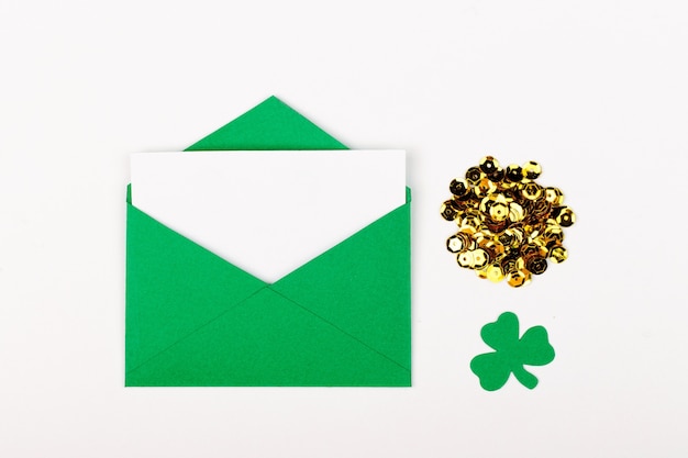 St. Patrick 's Day concept. Flat lay stylish set: empty card with green envelope and gold confett and clover leafi. Mockup template. View from above