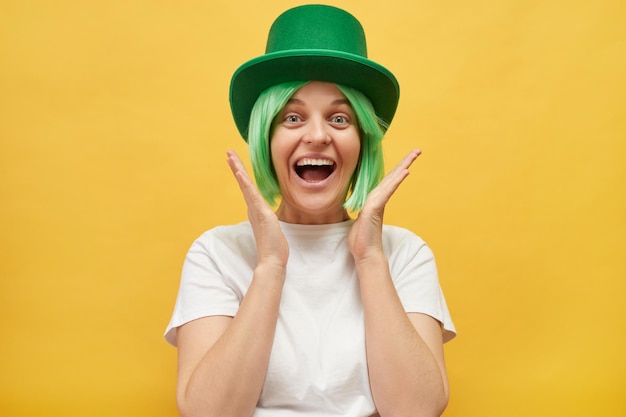 St Patricks Day festivities Extremely happy Caucasian woman wearing green leprechaun hat standing isolated over yellow background exclaiming with happiness