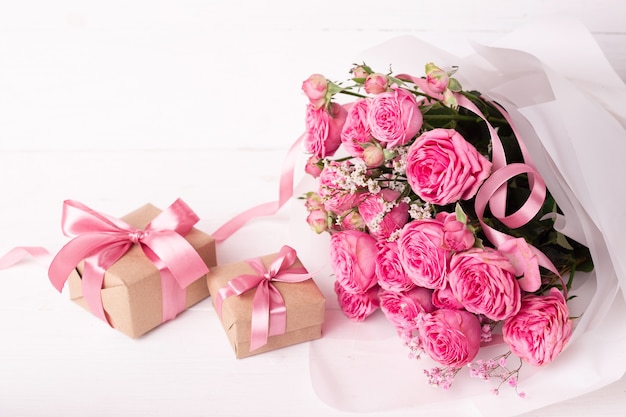 St. Valentines Day concept. Pink roses and gift boxes with ribbons on white wooden table.