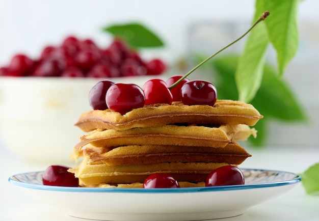 Stack of baked Belgian waffles with ripe red cherries on the white table