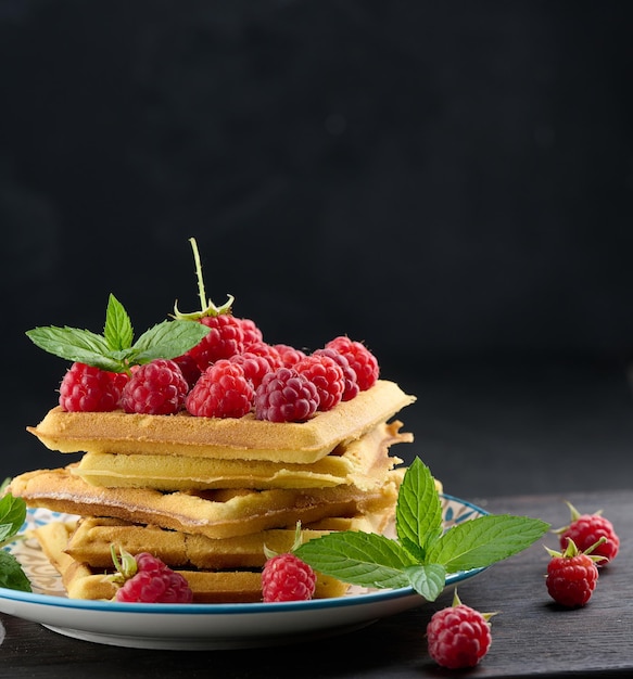 Stack of baked Belgian waffles with ripe red raspberry green mint leaves