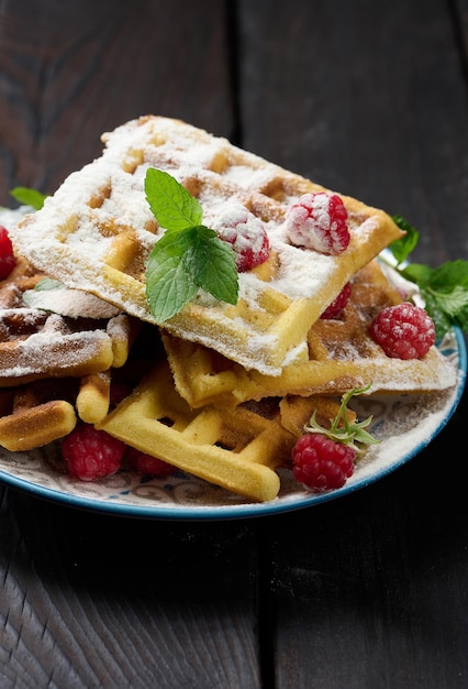 Stack of baked Belgian waffles with ripe red raspberry sprinkled with powdered sugar breakfast