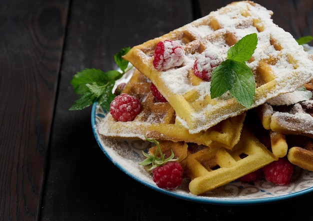 Stack of baked Belgian waffles with ripe red raspberry sprinkled with powdered sugar breakfast