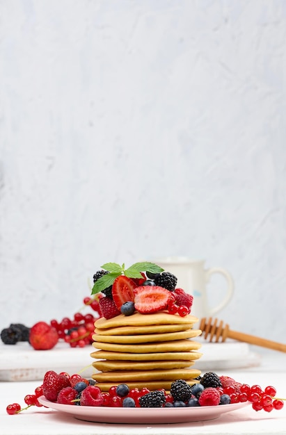 Stack of baked pancakes with fruits in a round plate on a white table delicious breakfast