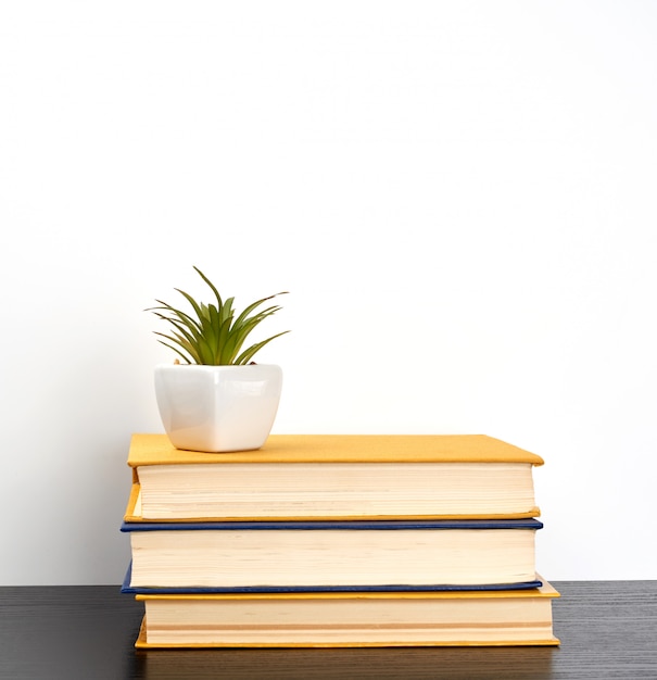 Stack books on a black table, on top a ceramic pot 