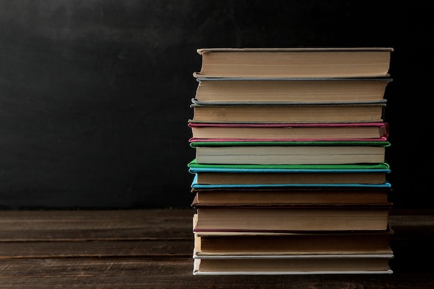 A stack of books on a brown wooden table and on a black background. Old books. Education. school. study With space for inscriptions