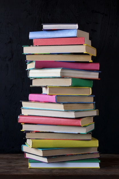 Stack of books in the colored cover on the table in the background of a school blackboard.