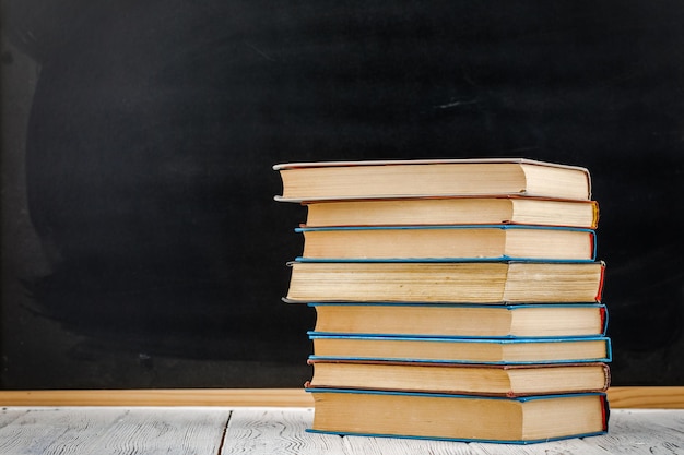 A stack of books on a white table against a blackboard.