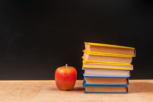 Stack of books with apple and pencil on table