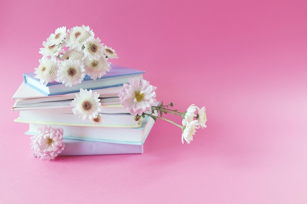 A stack of books with bookmarks from fresh chrysanthemum flowers, on a pink background