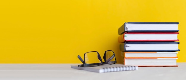 Stack of books with glasses on wooden desk on colorful yellow wall background