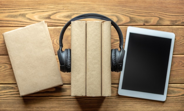 A stack of books with headphones and tablets on wooden background The concept of modern technological education and the study of books