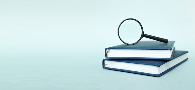 Stack of books with magnifying glass on turquoise background