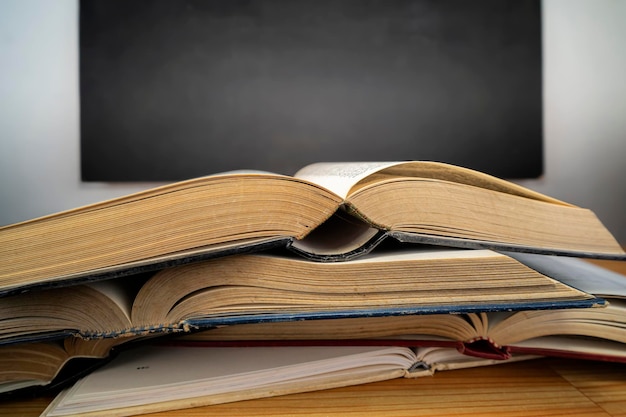 Stack of books with open book on wooden desk against blackboard background