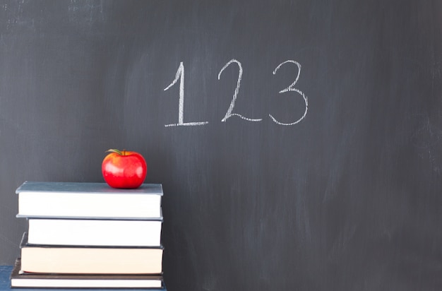 Stack of books with a red apple and a blackboard with "123" written on it