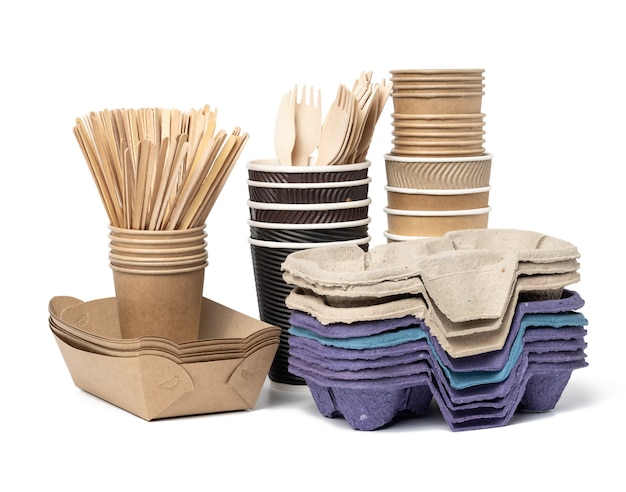 Stack of brown disposable paper cups, wooden forks and knives, plate on a white background. Utensils for takeaway drinks, zero waste