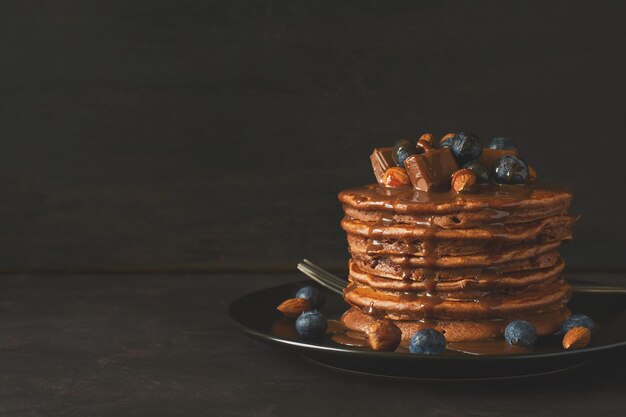 Stack of chocolate pancakes with icing blueberry almond hazelnut and pieces of chocolate Selective f